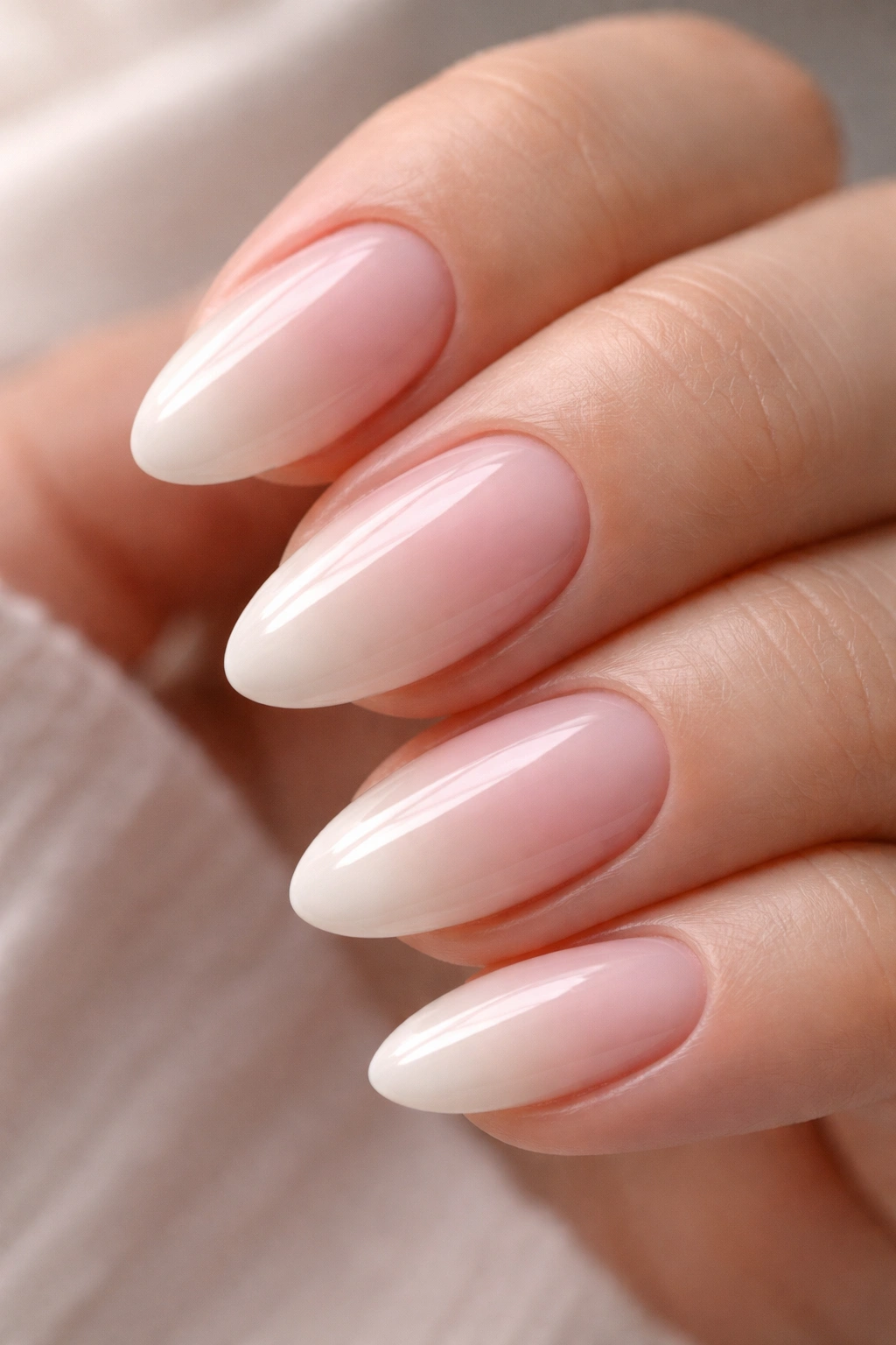 Close-up of short almond nails with a soft pink to white ombre gradient