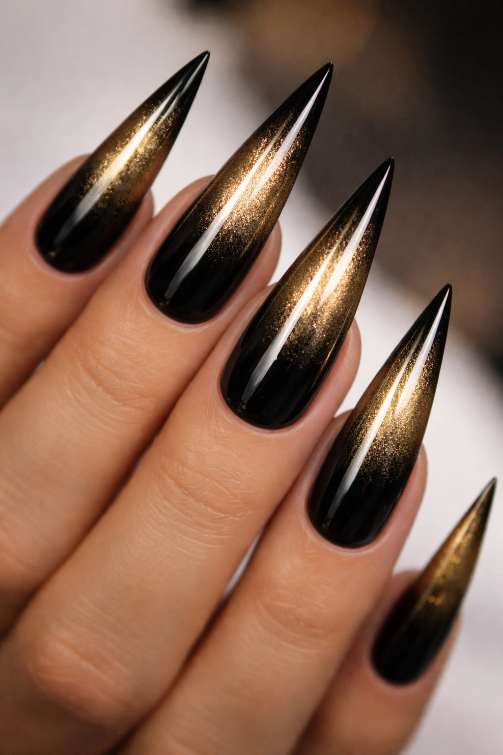 Close-up of black to gold ombré stiletto nails.