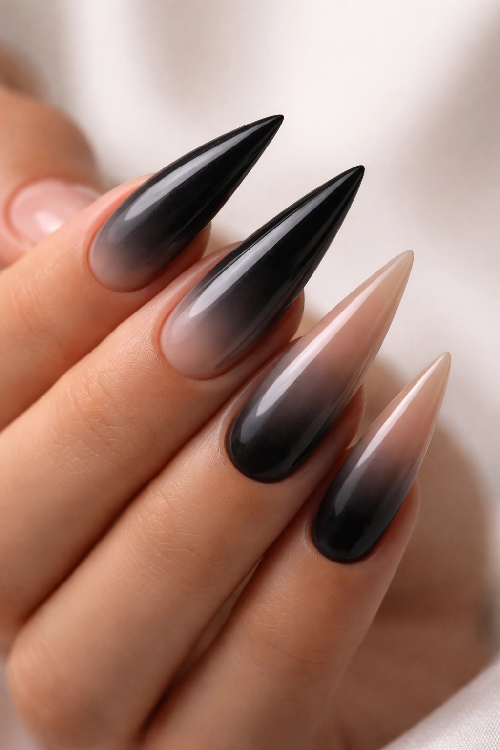 Stiletto nail with black to nude ombré gradient in studio lighting