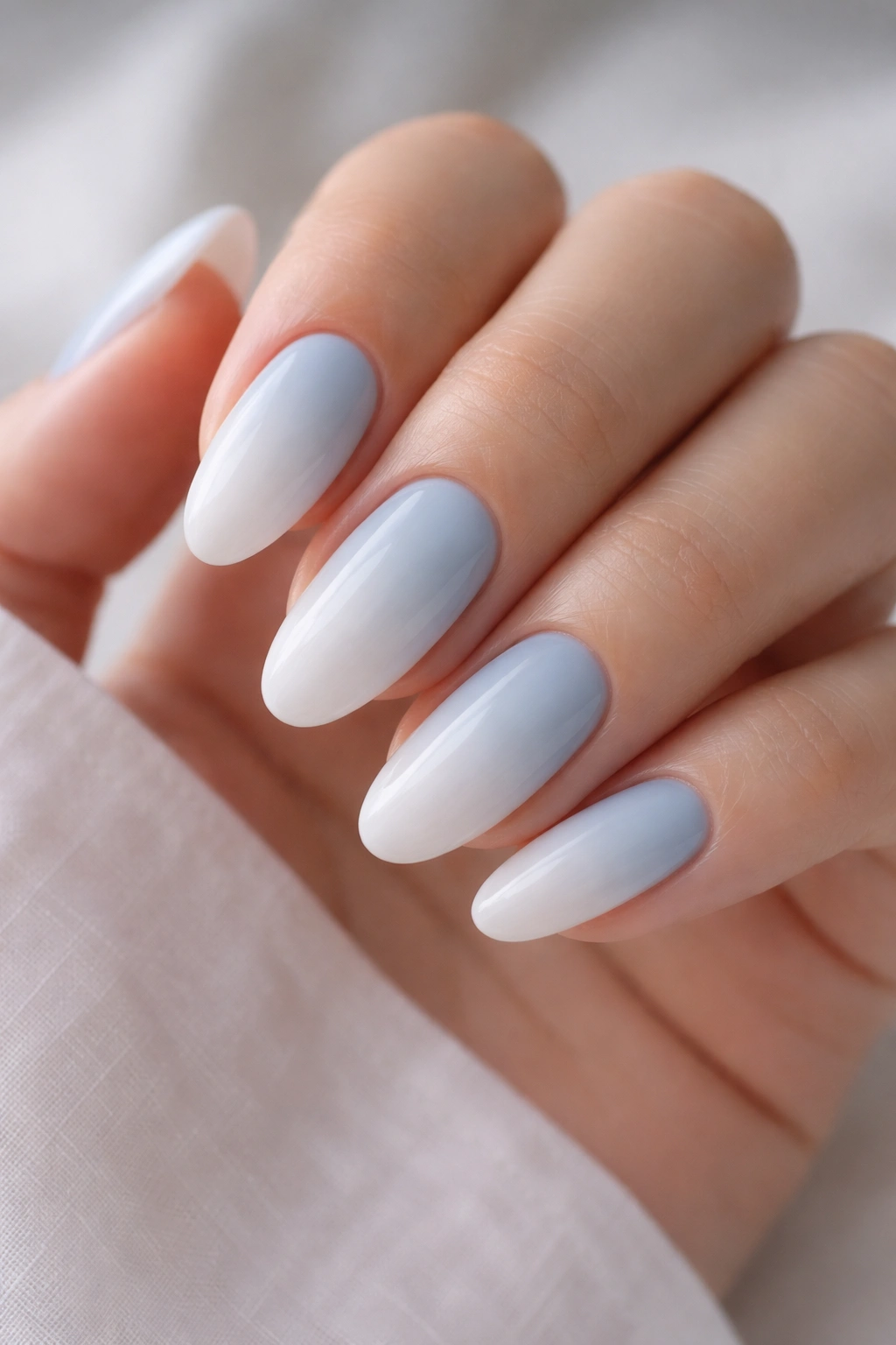 Close-up of long oval nails with pale blue to cloud white ombre in glossy gel