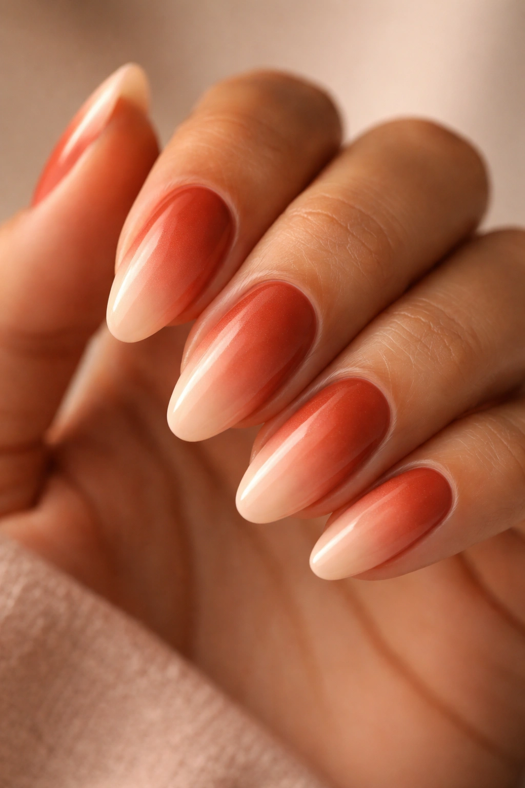 Almond nails gradient from burnt sienna to peach on a hand, warm studio lighting.