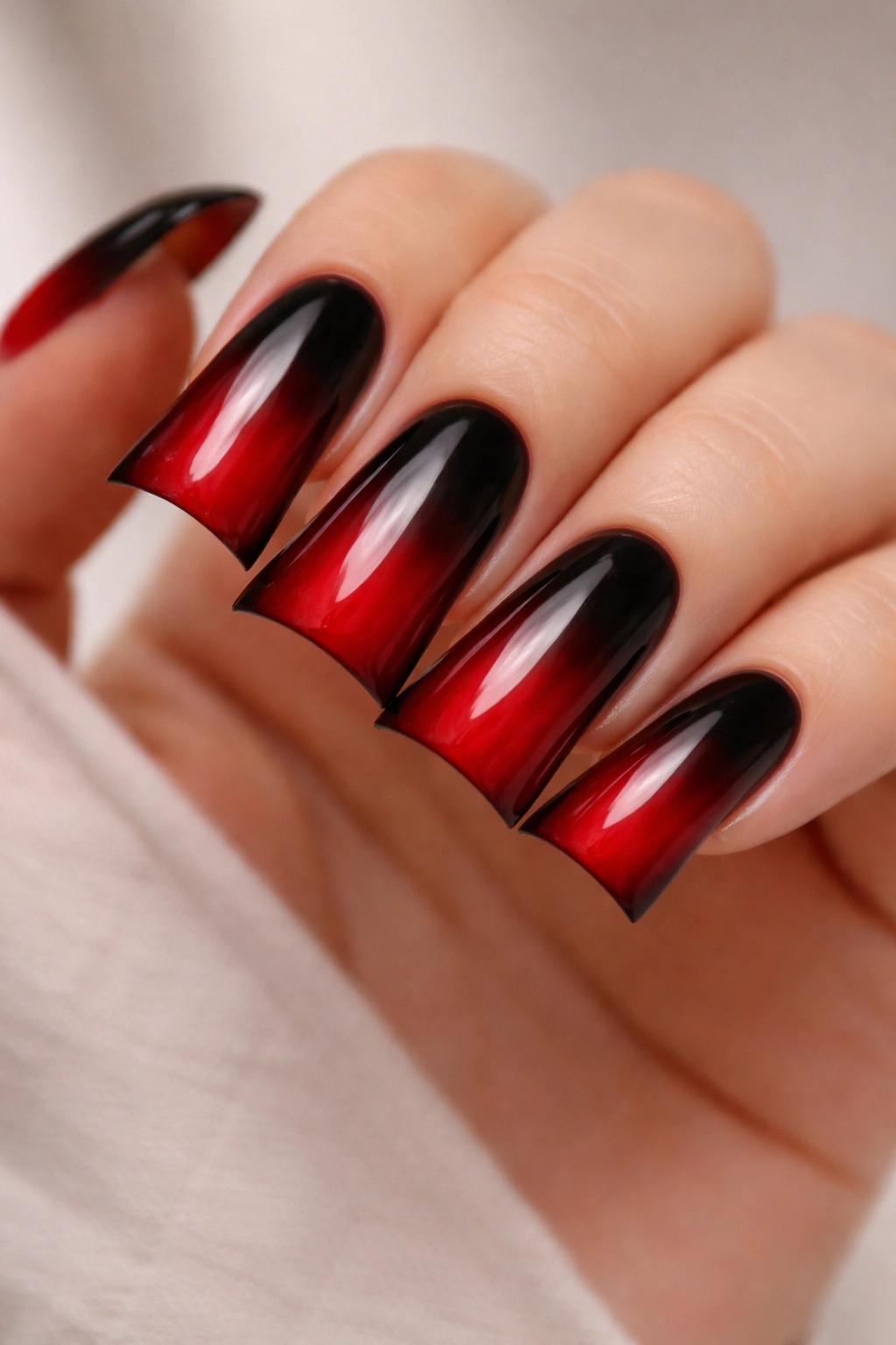 Close-up of duck nails with a black to red ombre gradient on curved tips