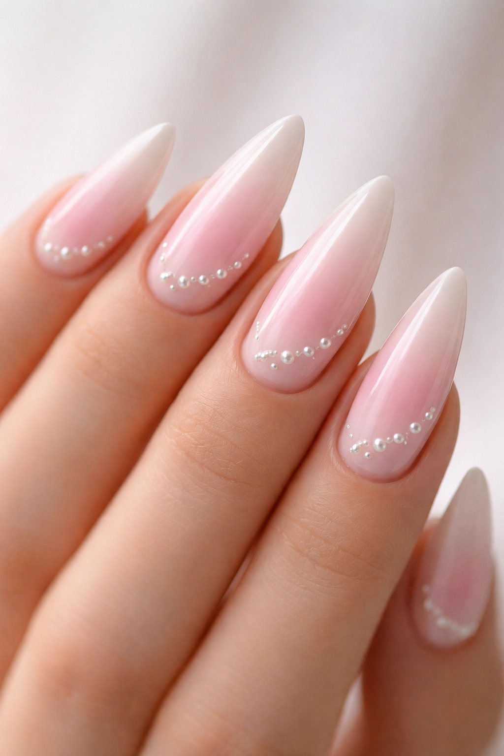 Baby pink ombre stiletto nails with pearl beads along the gradient on medium-length nails