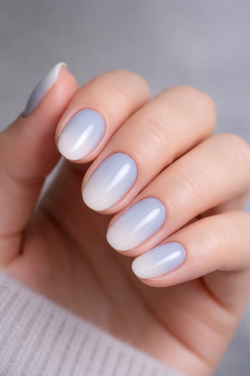 Close-up of short oval nails in powder blue to cloud white ombre