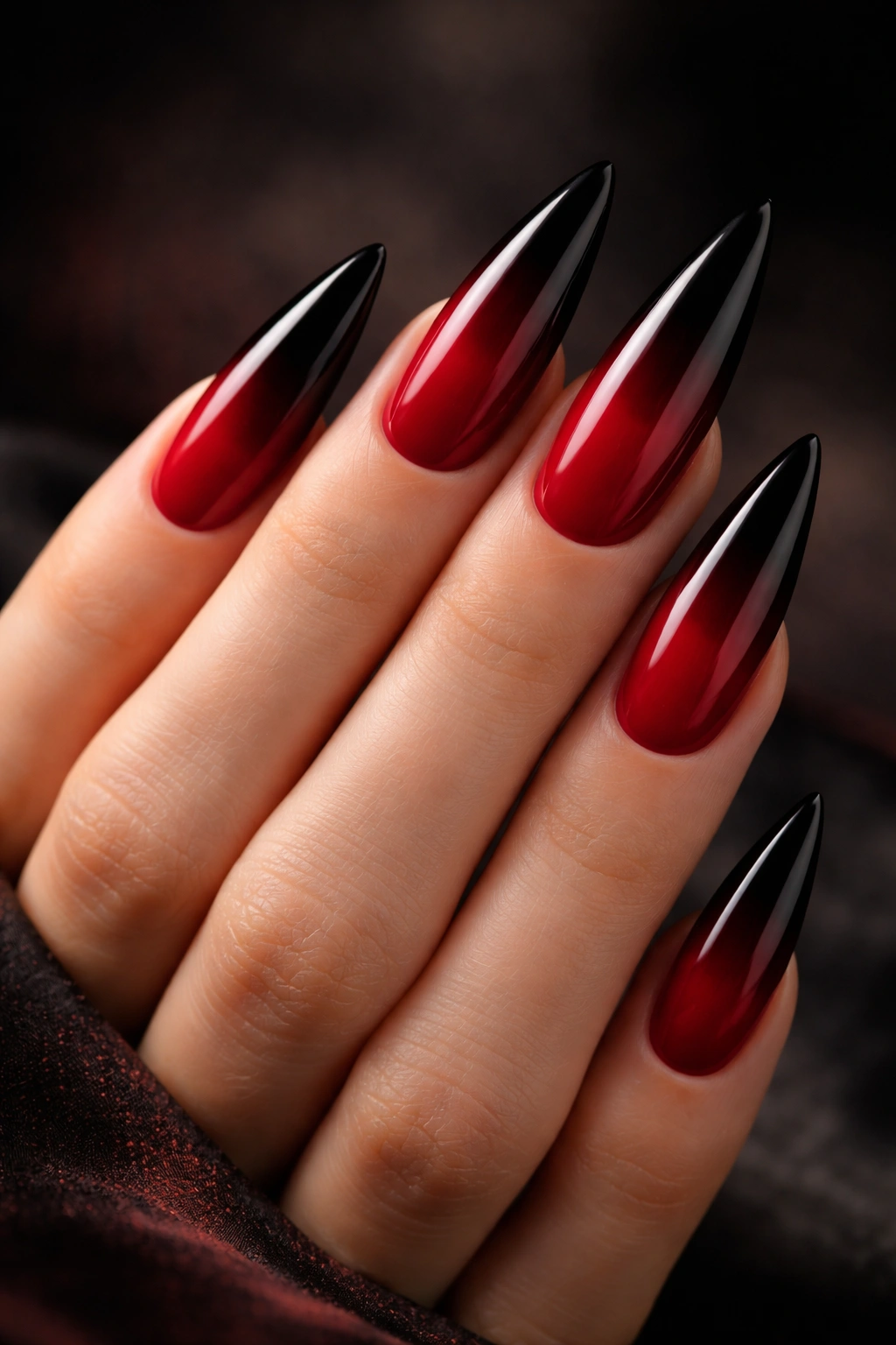 Close-up of ombré red to black stiletto nails on a neutral background