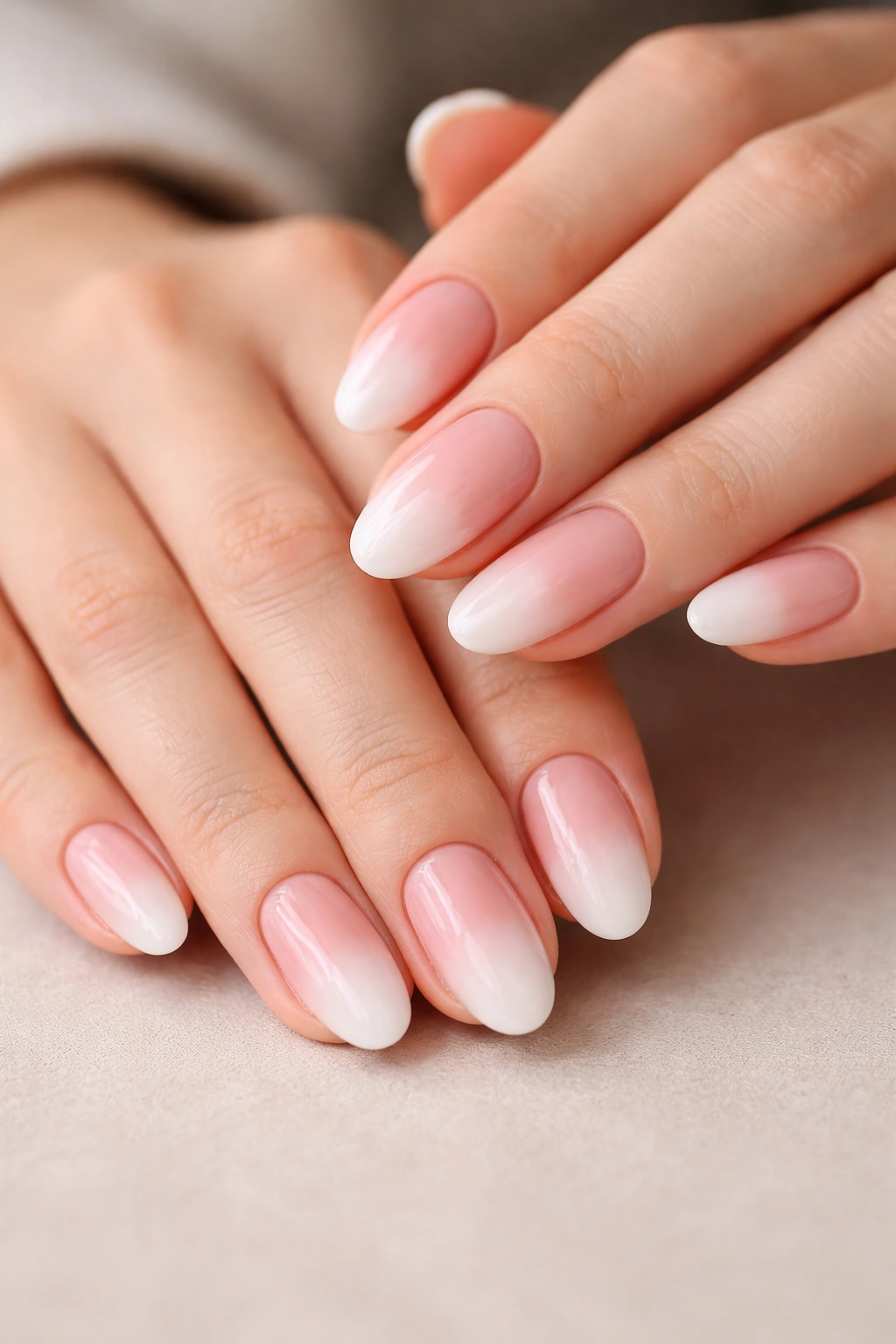 Close-up of short almond nails in a pink to white gradient on a natural-toned hand