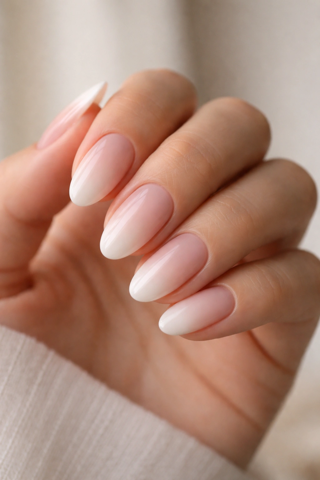 Close-up of short almond nails with a nude-to-milky-pink ombre gradient