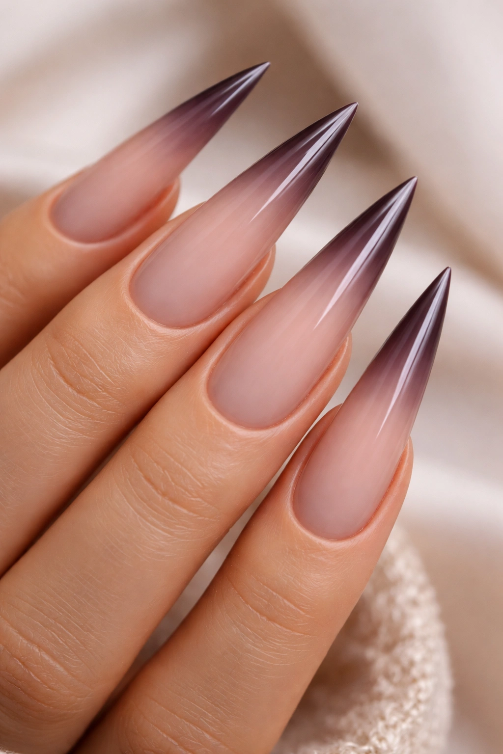 Close-up of elongated stiletto nails with a soft pink to burgundy ombré gradient on a hand