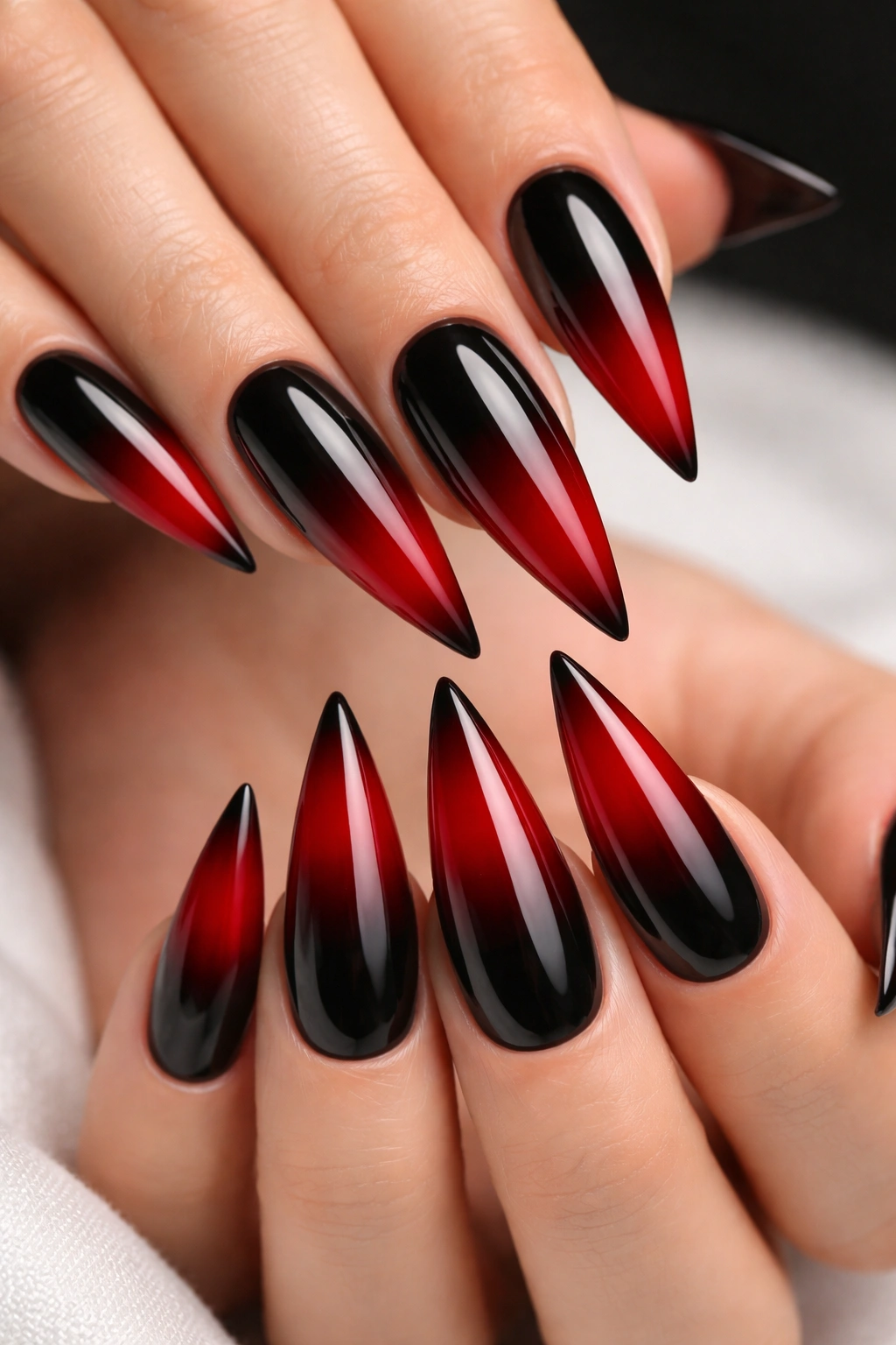 Close-up of black-to-red gradient stiletto nails with glossy finish on a neutral background