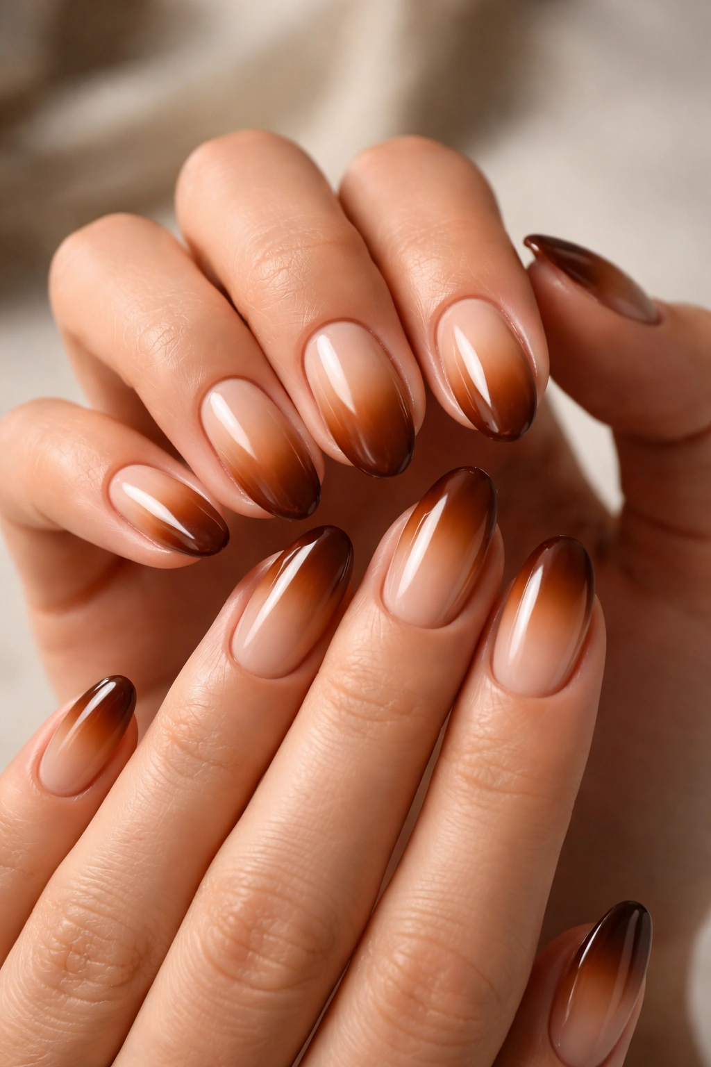 Close-up of short almond nails with nude-to-saddle-brown ombré gradient and glossy finish