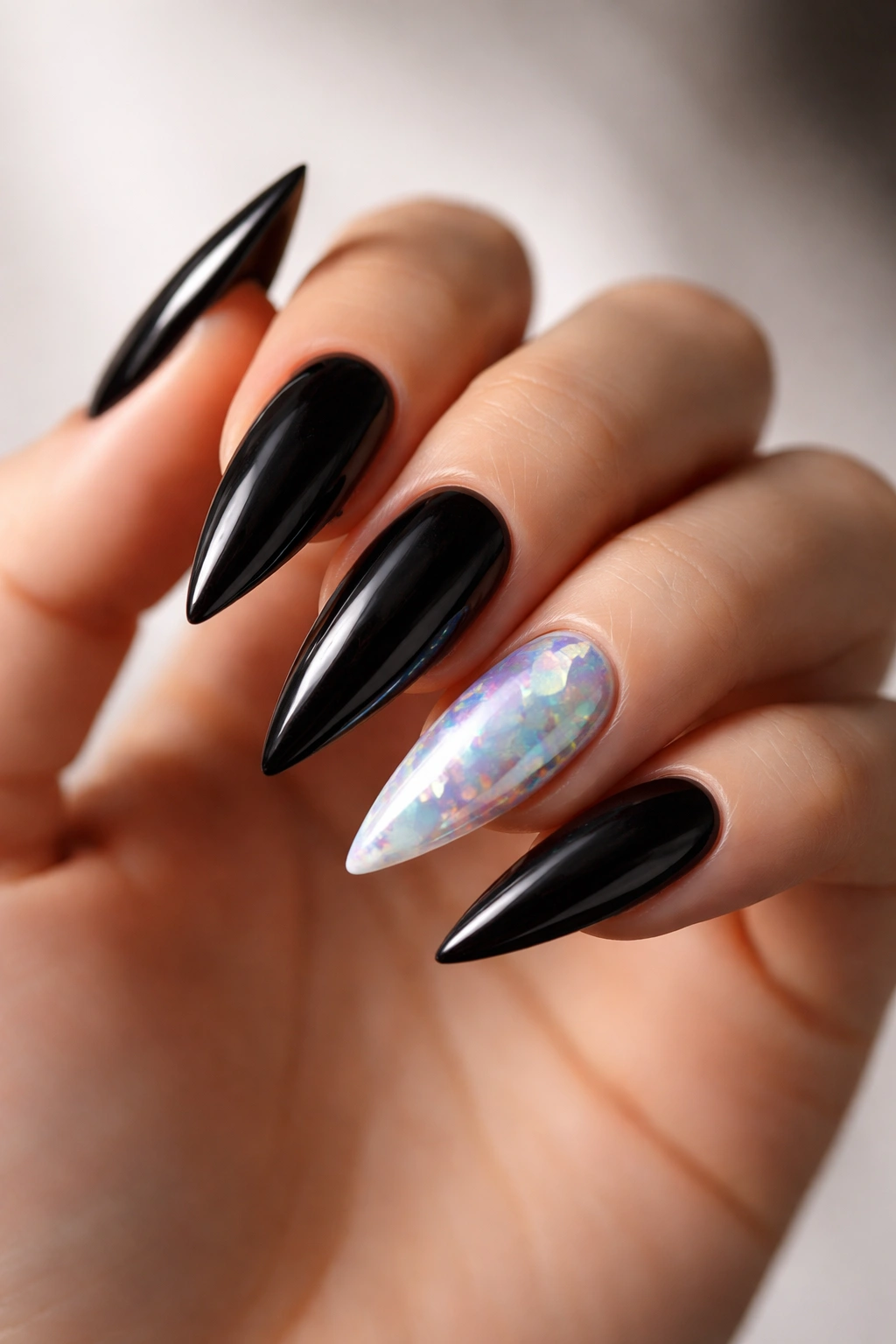 Close-up of black stiletto nails with opal-accent nails showing color-shifting blues greens pinks.