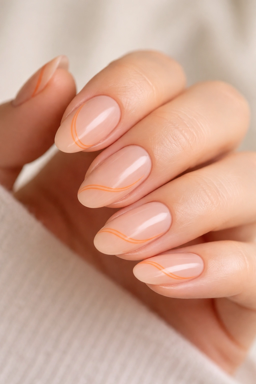 Close-up of short almond nails with delicate orange line art on a nude base.