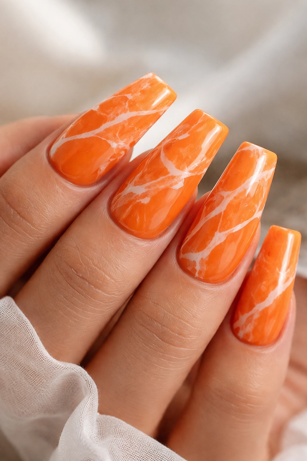 Close-up of orange duck nails with white marble veins