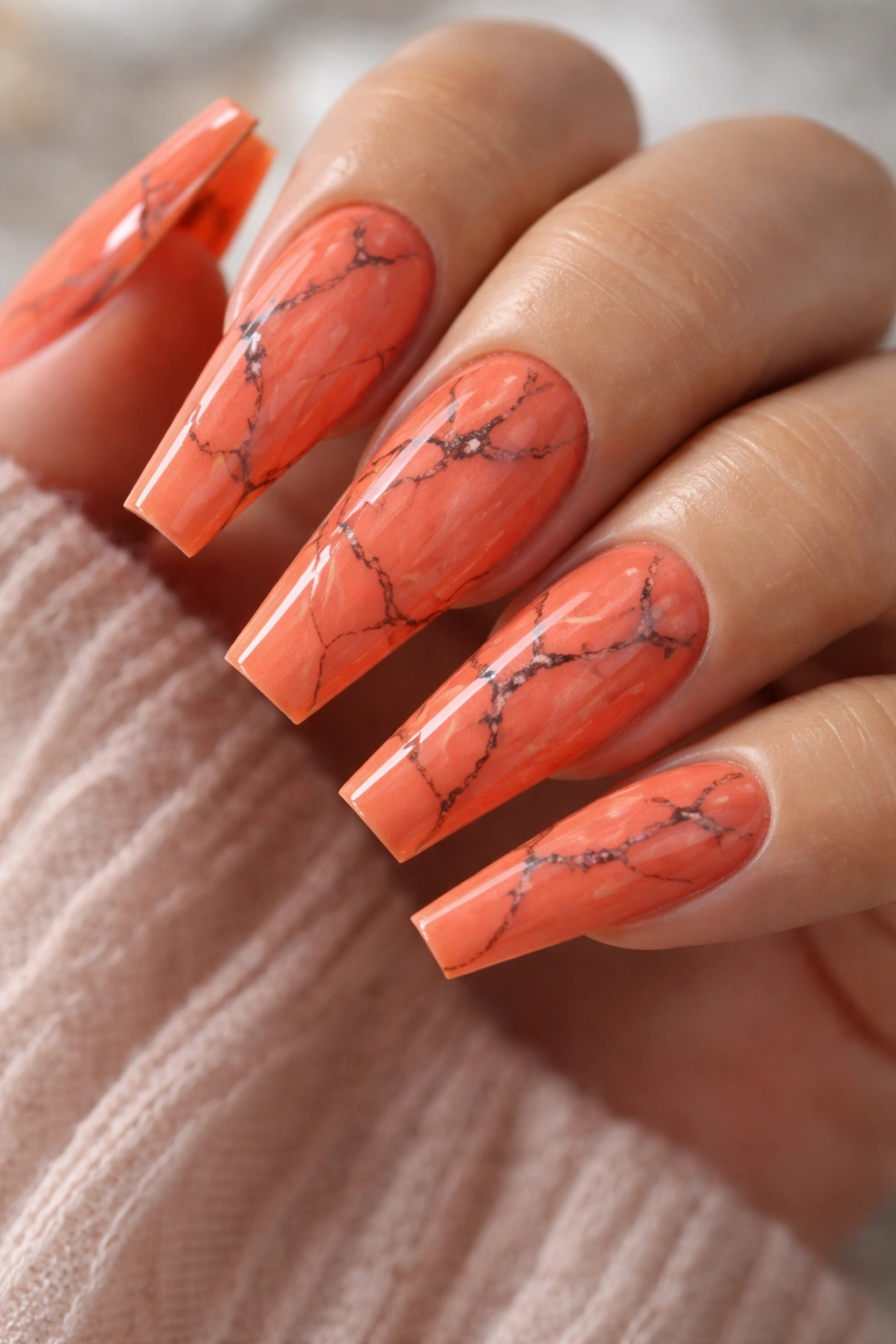 Close-up of coffin nails featuring coral-orange marble with delicate dark veins.