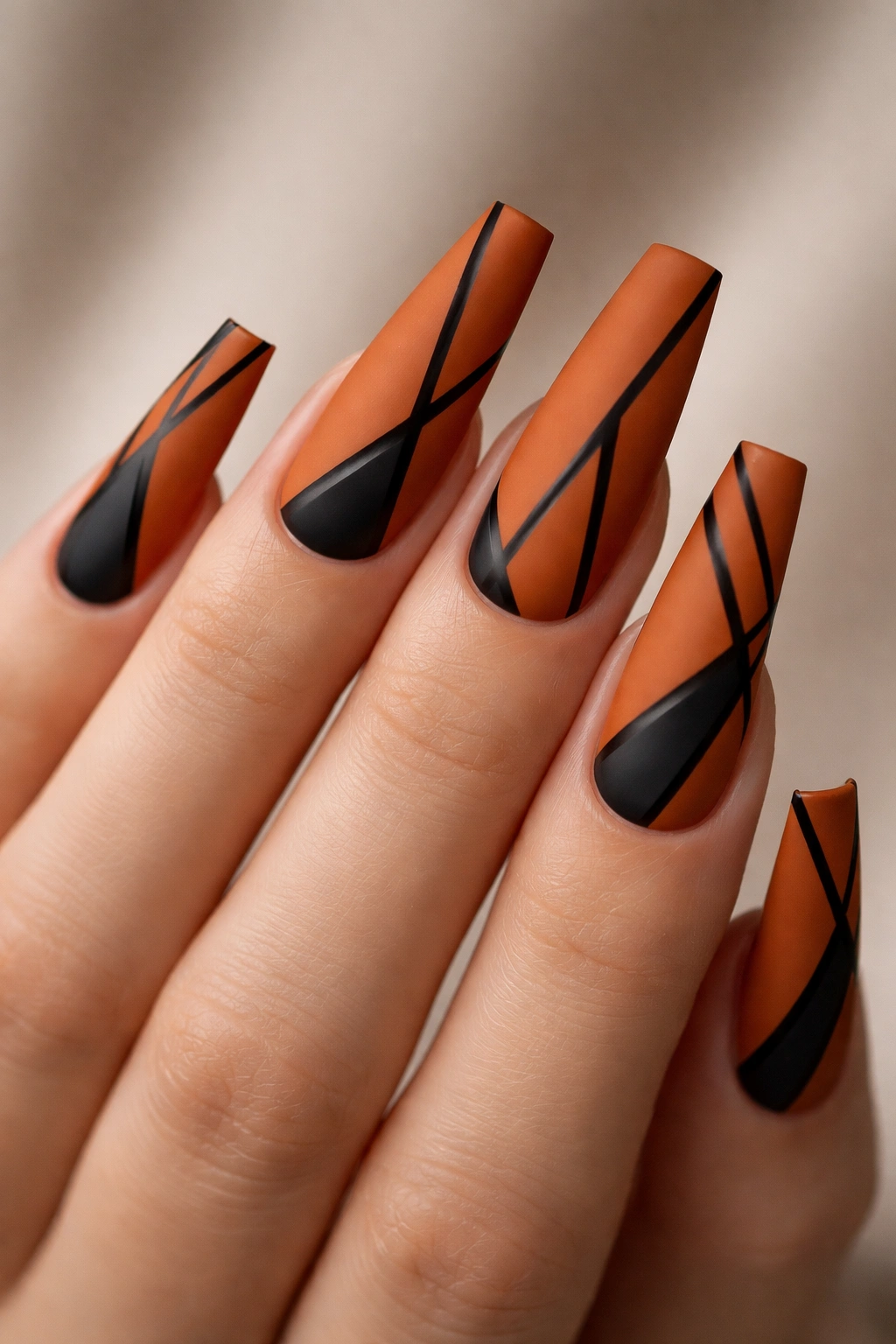 Long coffin nails in burnt orange matte with black geometric patterns.