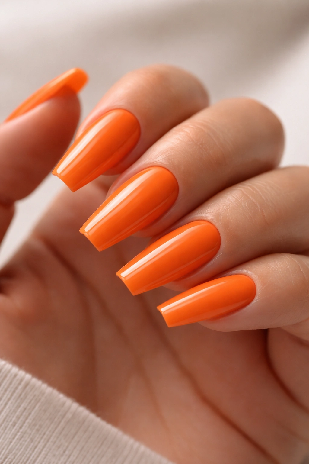 Close-up of ballerina nails with sharp orange polish