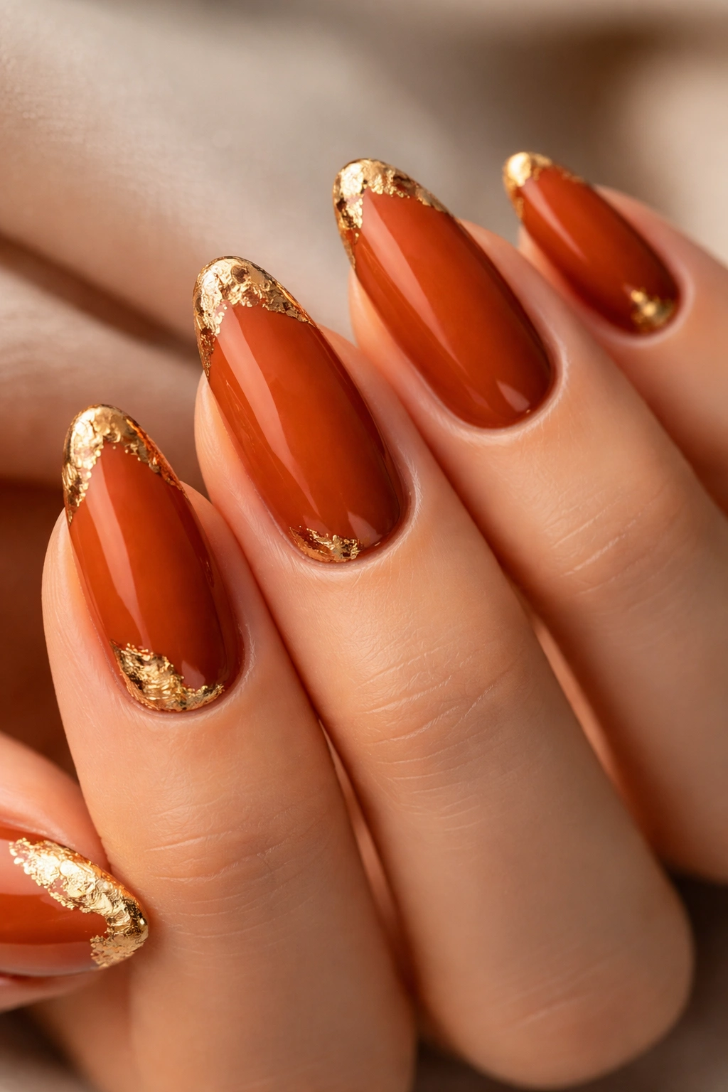 Close-up of burnt orange nails with gold foil accents