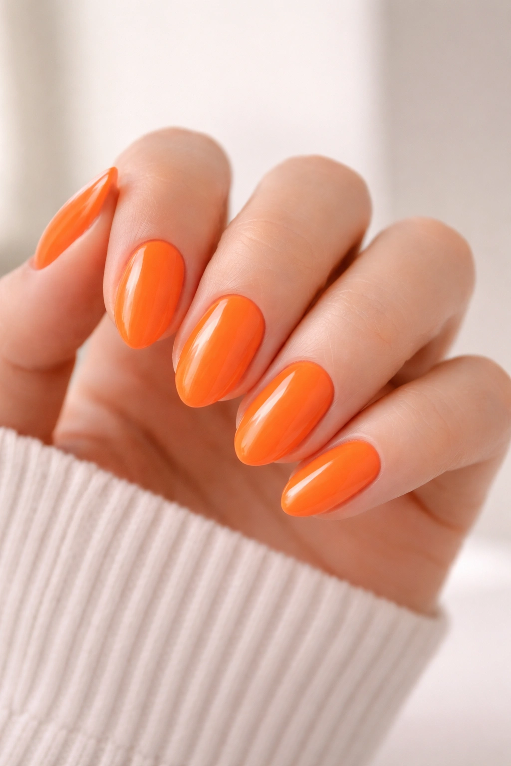 Close-up of short almond nails in bright orange with crisp glossy finish