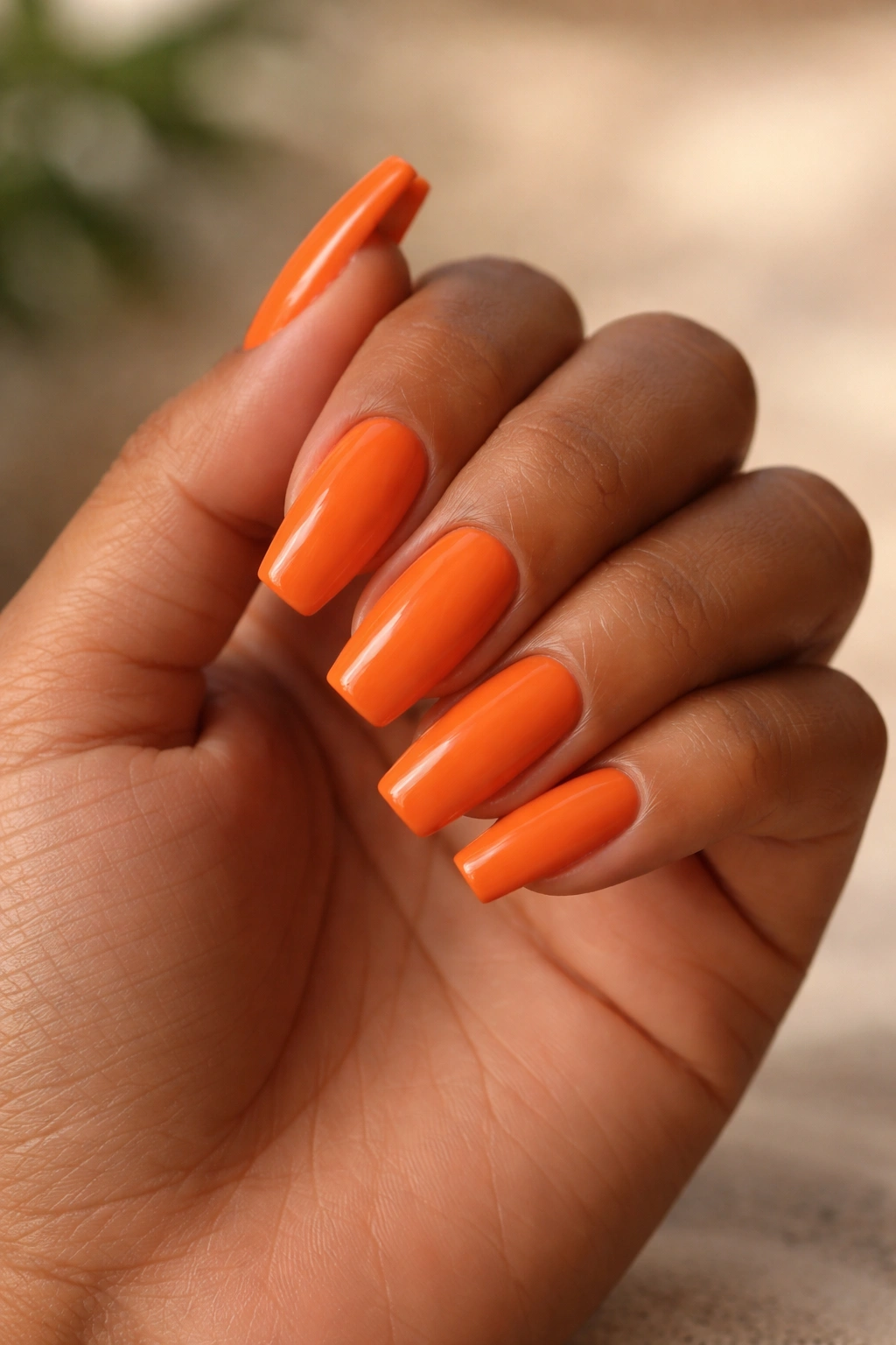 Close-up of medium-length ballerina nails in warm orange against medium skin tone