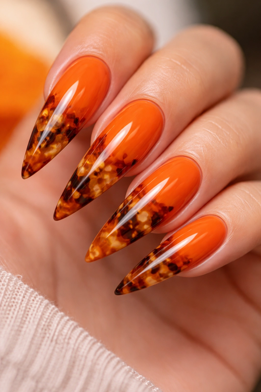 Close-up of orange stiletto nails with tortoiseshell pattern.