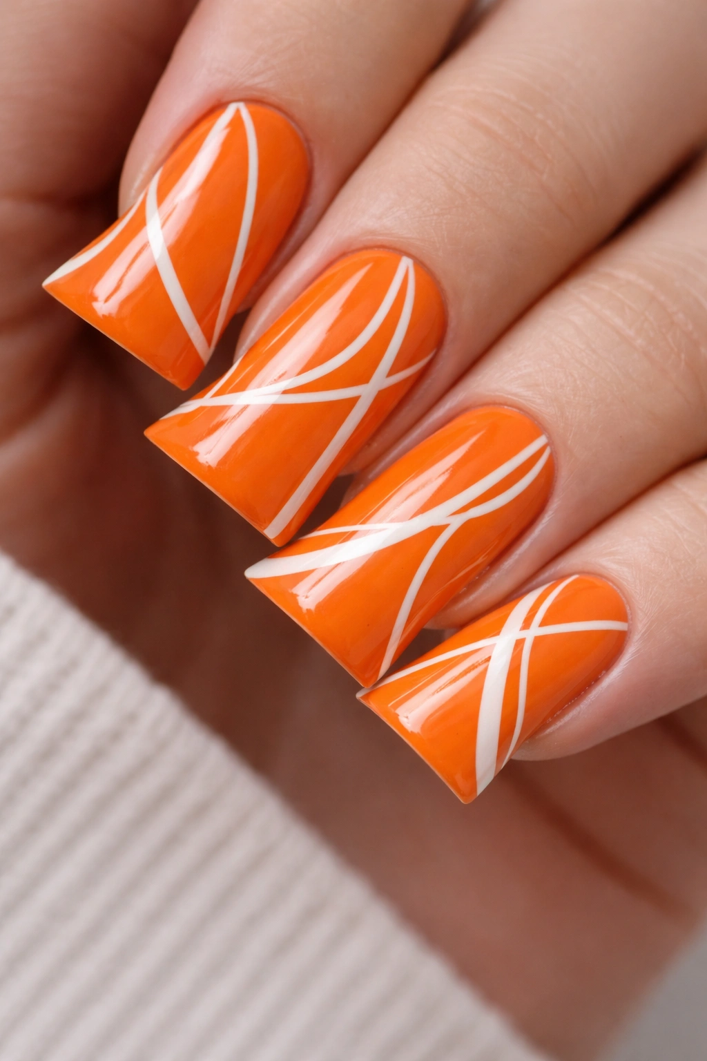 Close-up of orange duck nails with white geometric lines