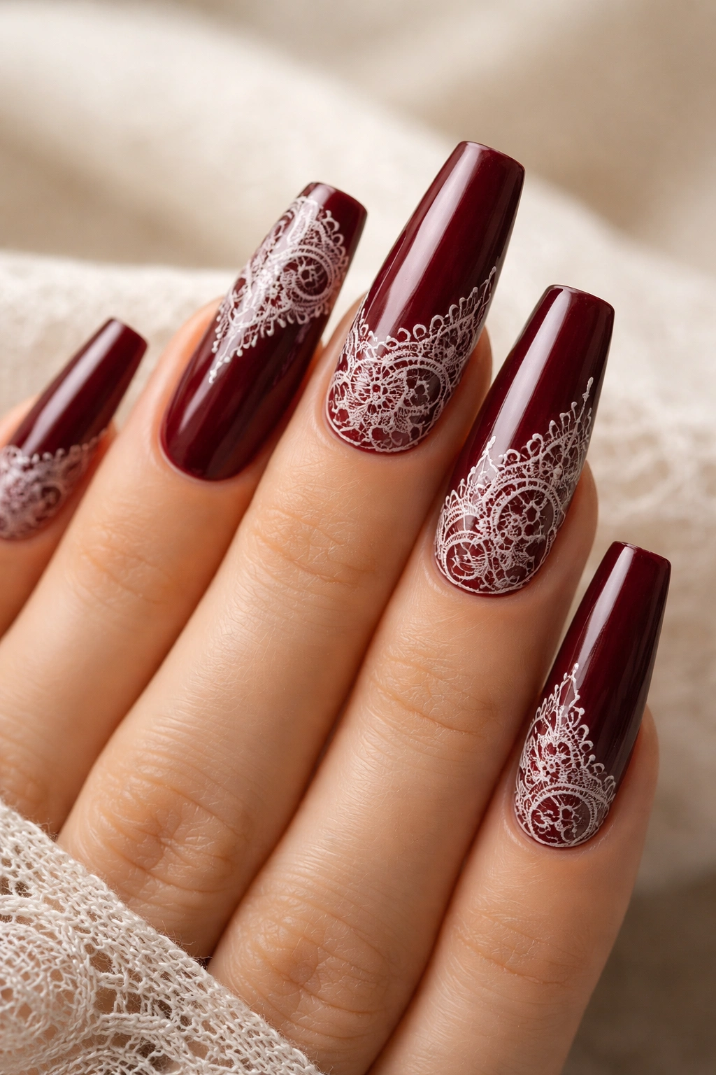 Close-up of oxblood coffin nails with white lace stamping showcasing intricate lace on a dark red base