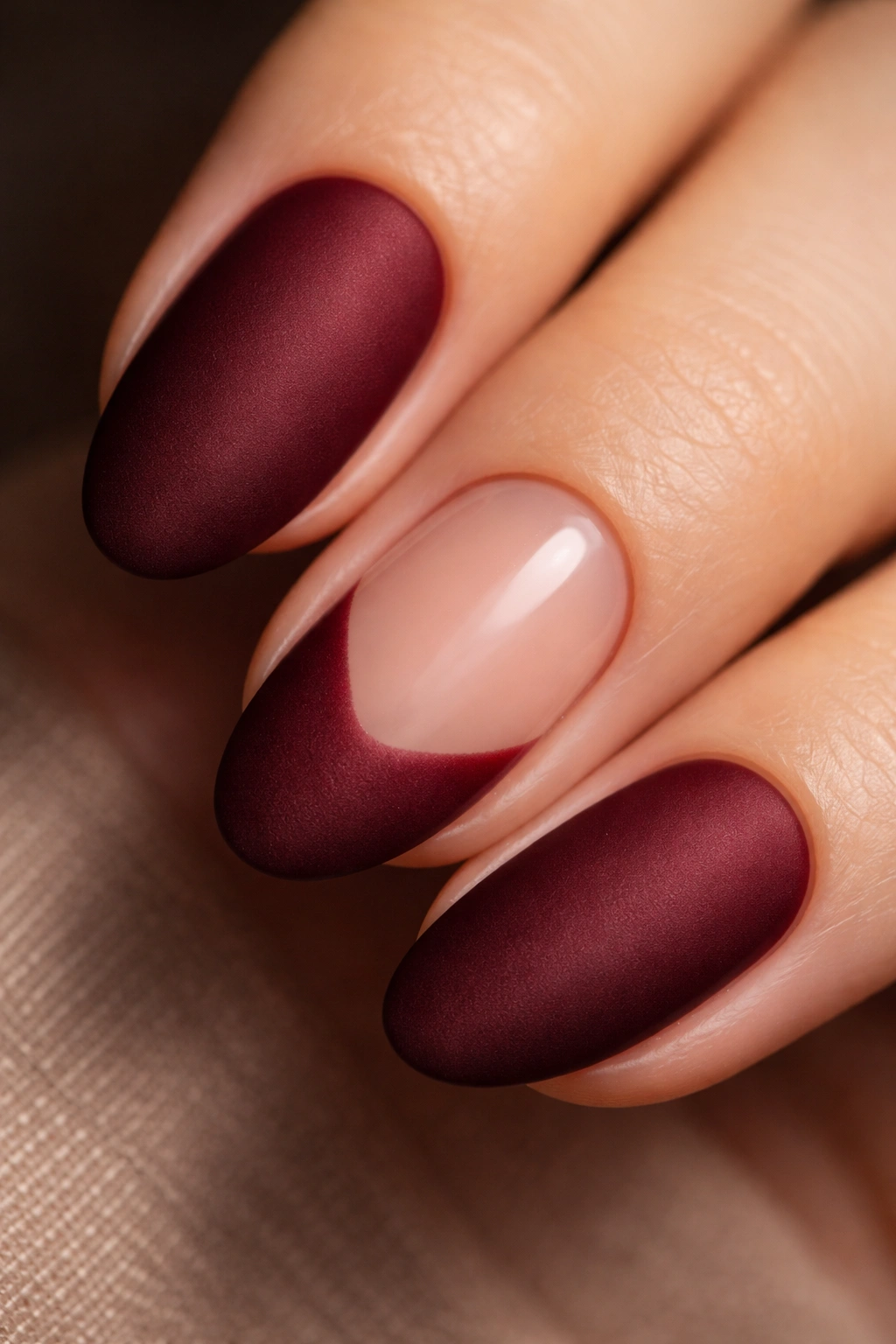 Oxblood matte nails on short almond shape with one bare accent nail