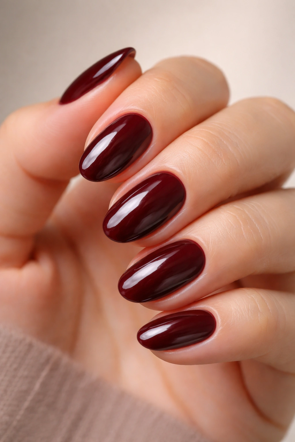 Close-up of oxblood maroon short oval nails with a glossy finish on a bare hand