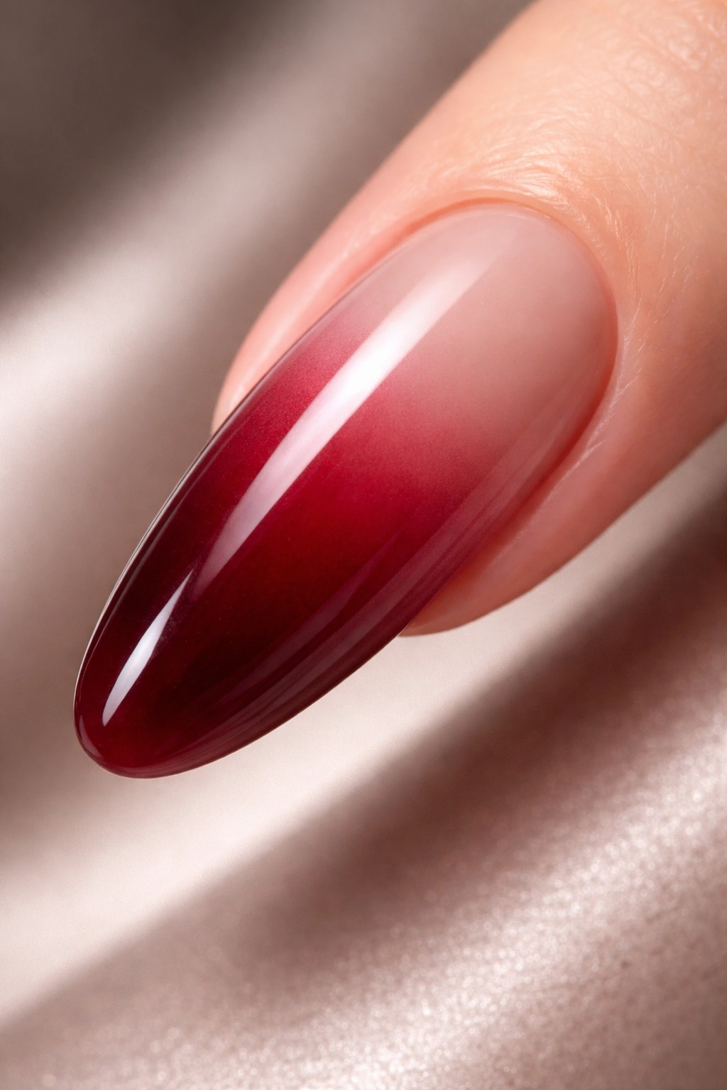 Close-up of a long round acrylic nail with oxblood red blending into nude under studio lighting