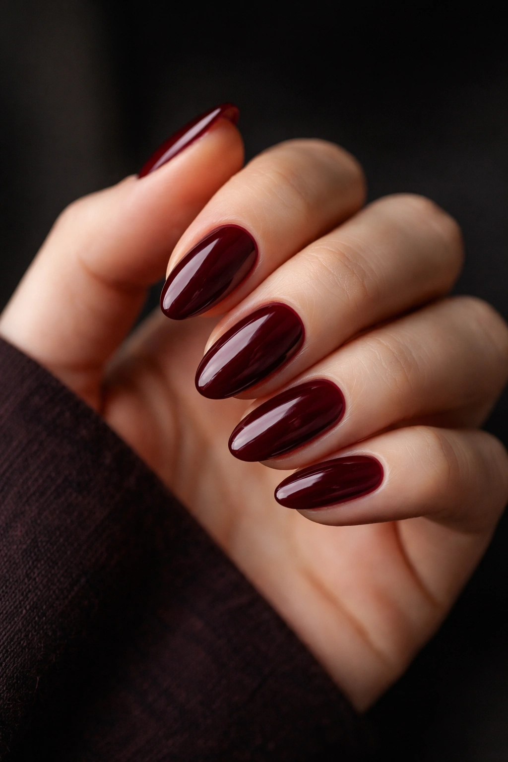 Close-up of short almond nails in oxblood red with glossy finish