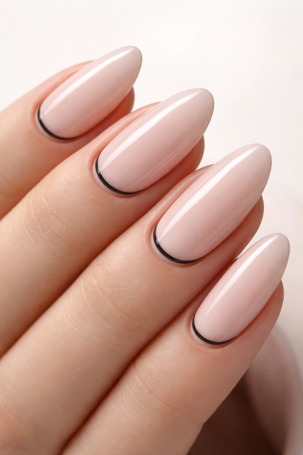 Close-up of long oval nails with pale blush polish and a thin charcoal base line near the cuticle.