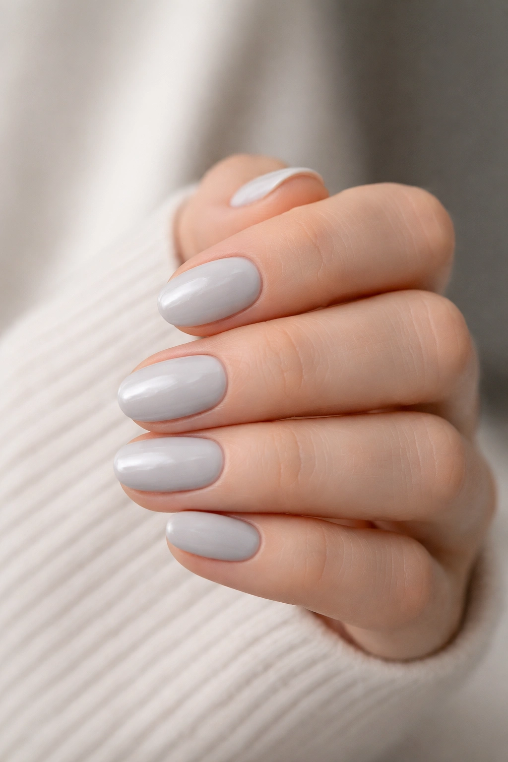 Close-up of a hand with pale gray short oval nails on a neutral background