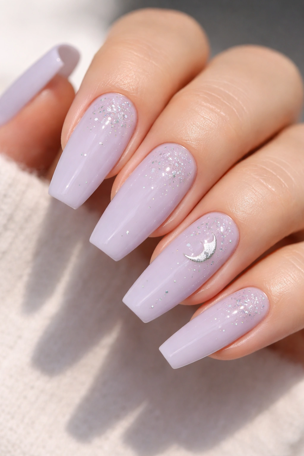 Close-up of pale lavender nails with sparse celestial glitter on a neutral background