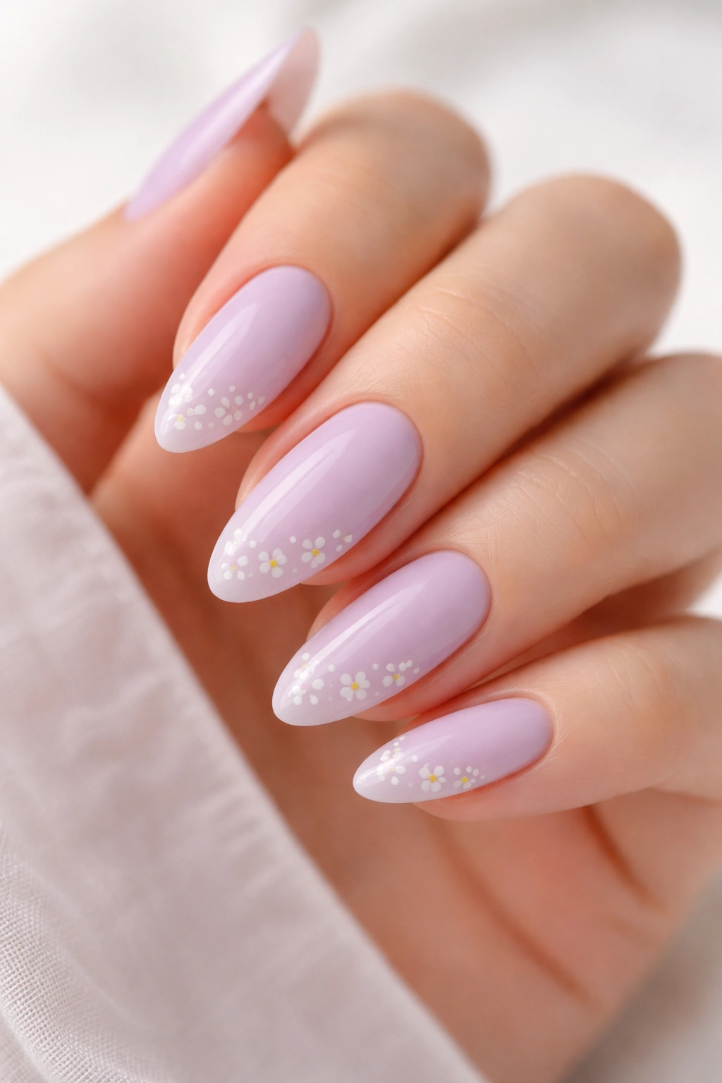 Close-up of pale lilac almond nails with tiny white floral accents.