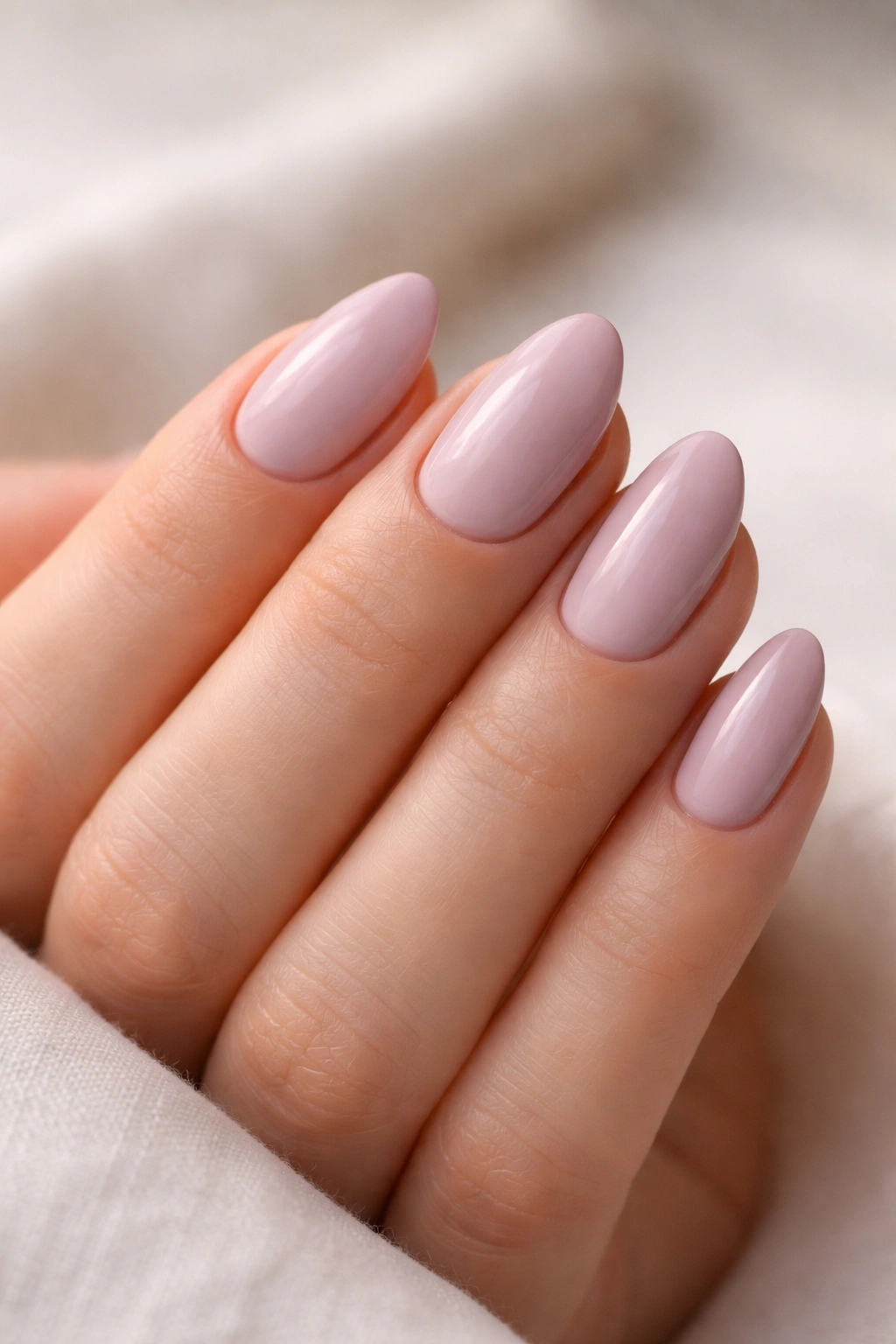 Close-up of a hand with pale mauve short almond nails on a neutral backdrop