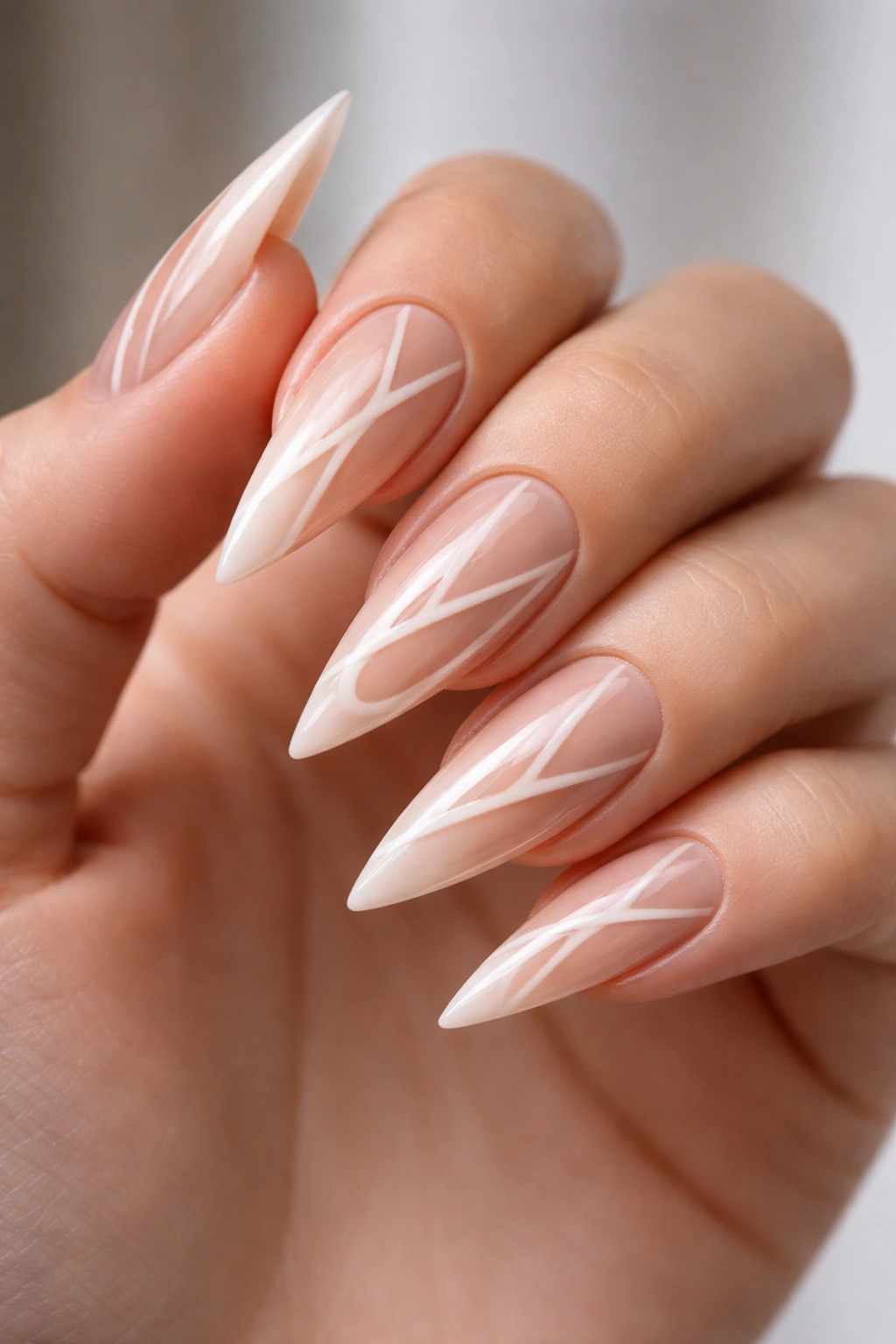 Close-up of pale nude stiletto nails with geometric negative-space pattern