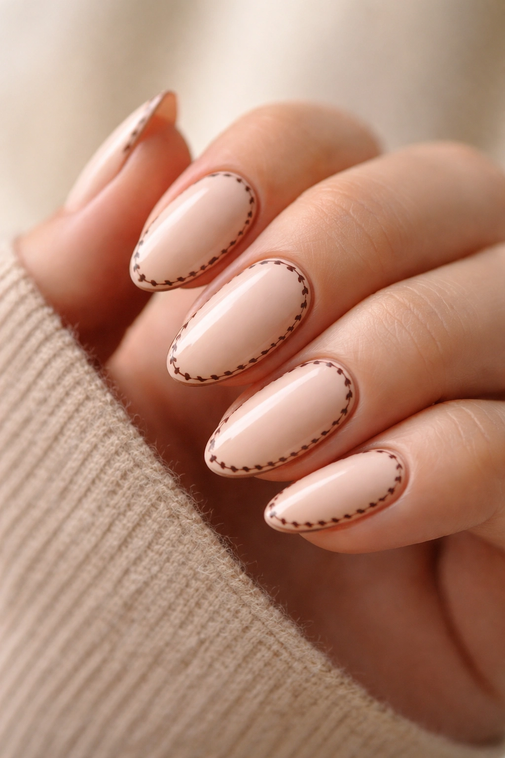 Close-up of pale peach short almond nails with brown stitch edging