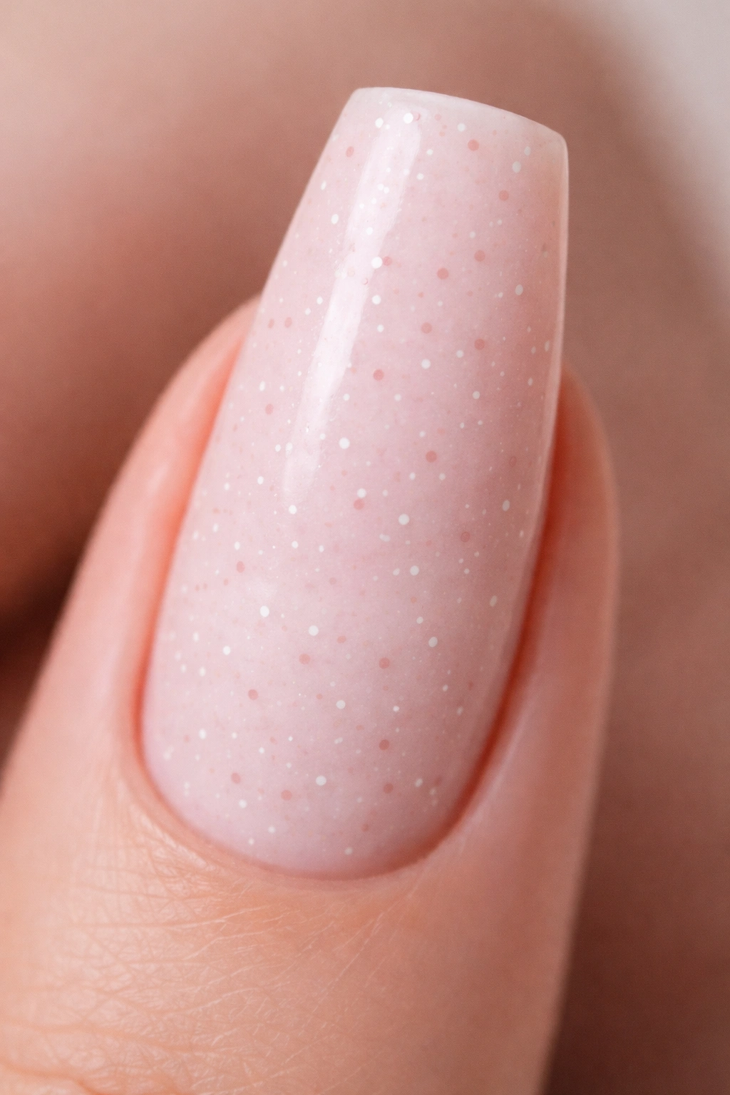 Close-up of pale pink coffin nail with micro-dot pattern on a soft backdrop