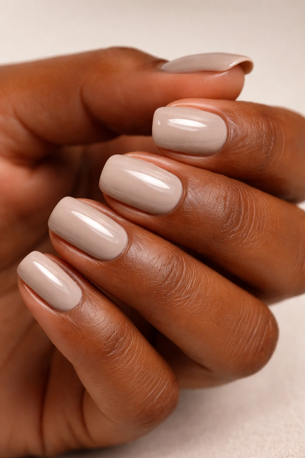 Close-up of short squoval nails painted pale taupe on deep skin
