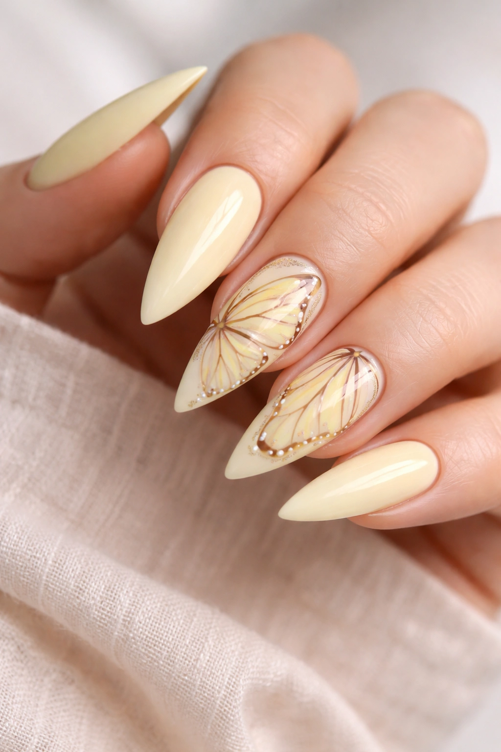 Close-up of stiletto nails with pale yellow base and butterfly wing designs