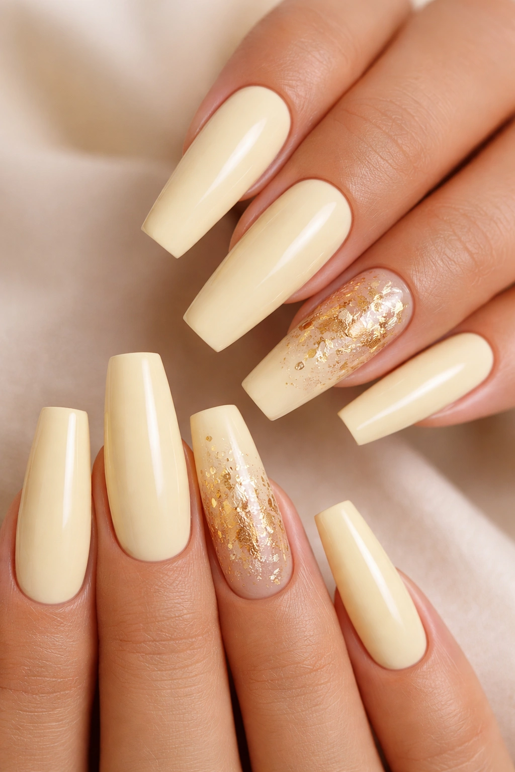 Close-up of pale yellow coffin nails with delicate gold leaf accents.