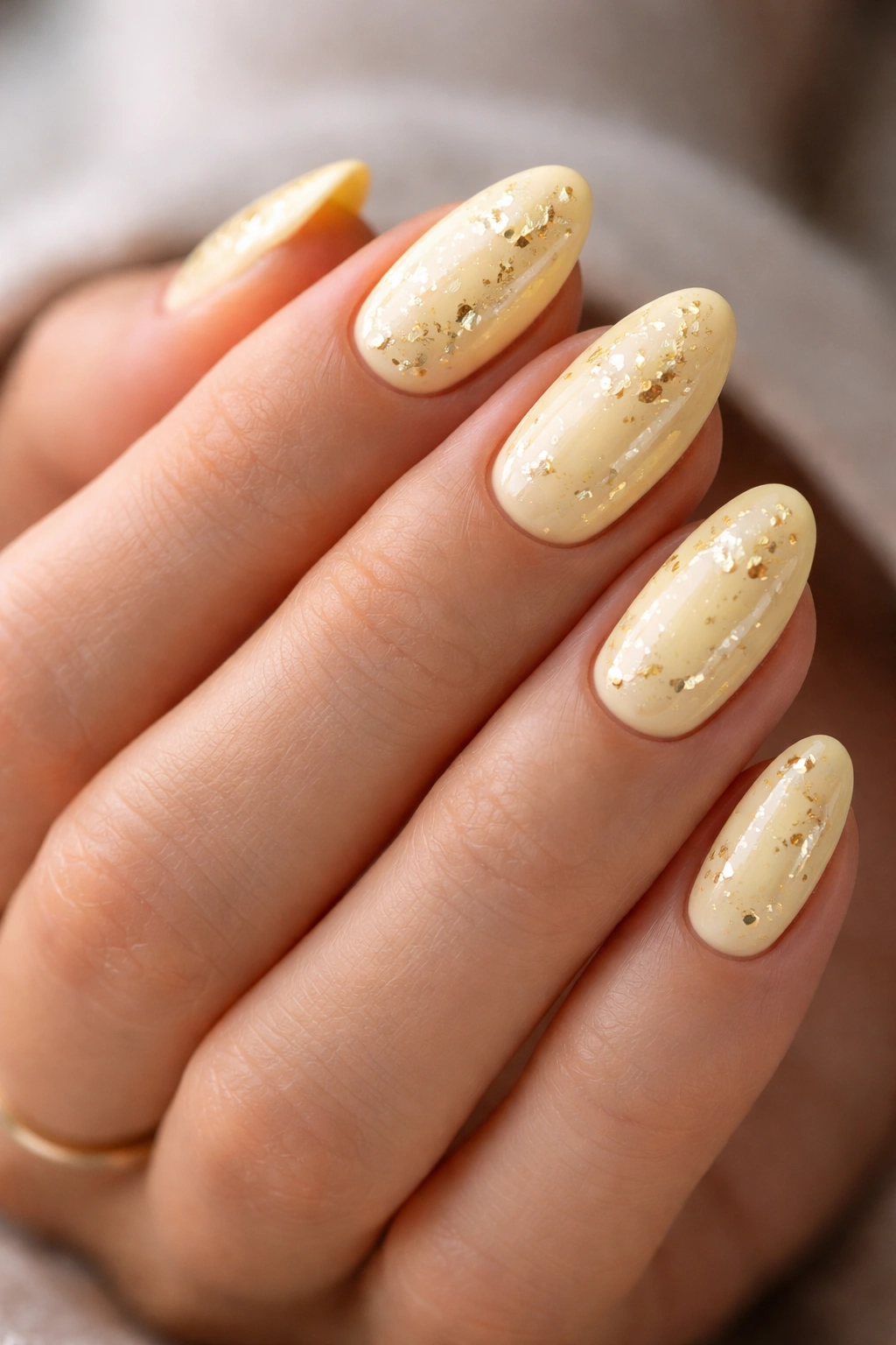 Close-up of pale yellow nails with small gold foil accents