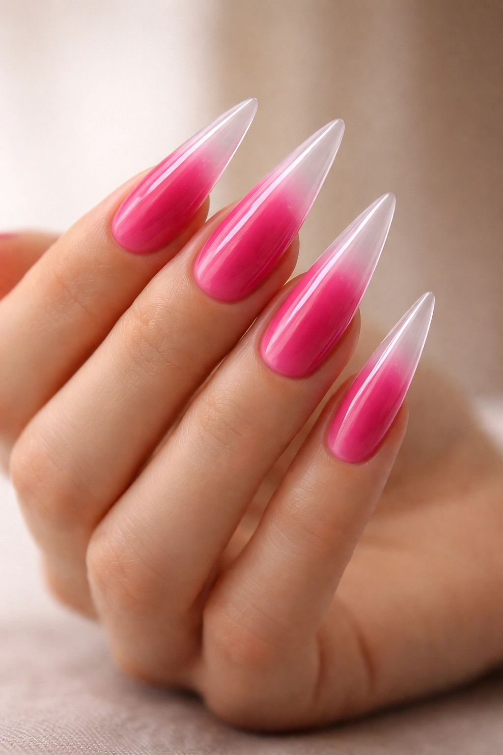 Close-up of a hand with long stiletto nails in vibrant pink fading to clear tips