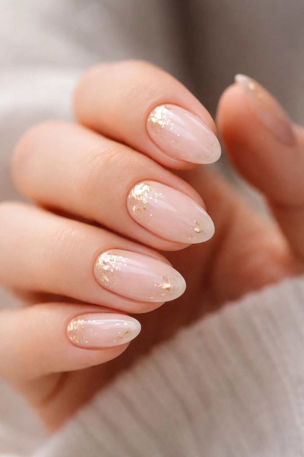 Close-up of pastel almond nails with tiny gold foil flecks on a soft pink base, studio lighting.