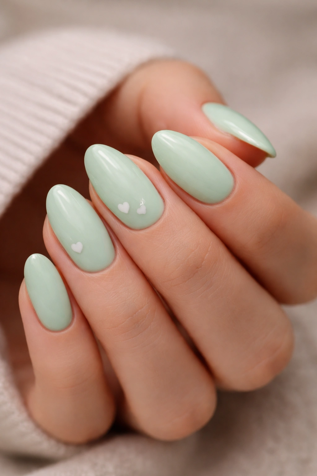 Close-up of pastel green almond nails with tiny white hearts.