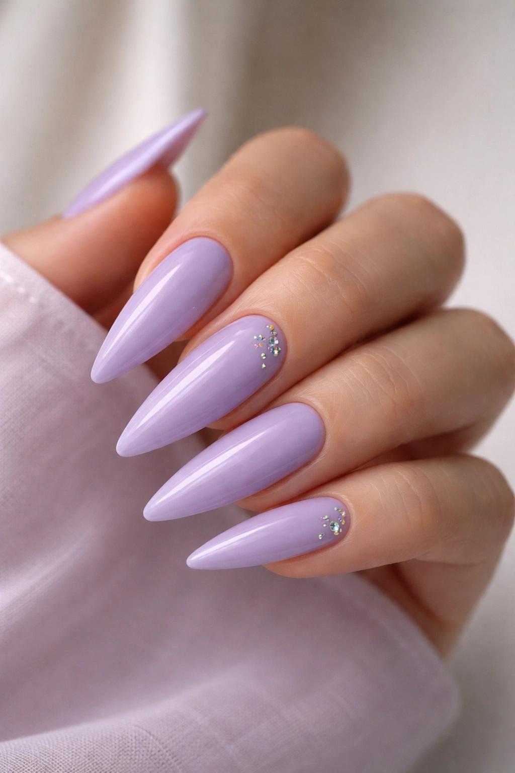 Close-up of pastel lavender nails with rhinestones on stiletto tips