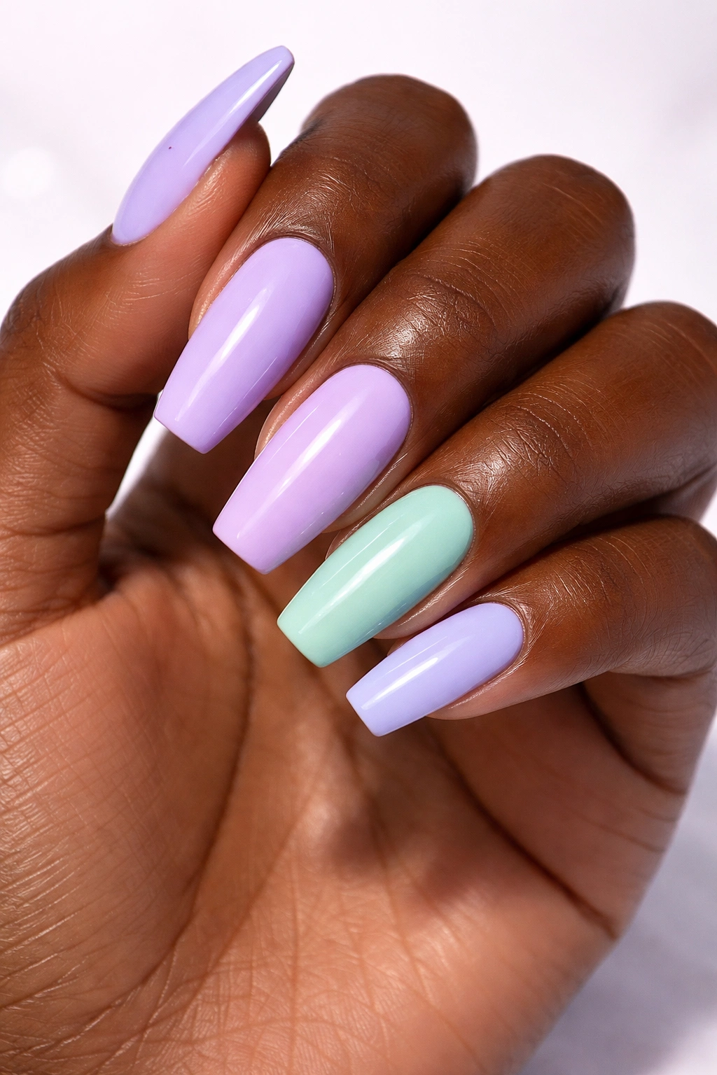 Close-up of a dark-skinned hand with lavender, lilac, and mint pastel nails.