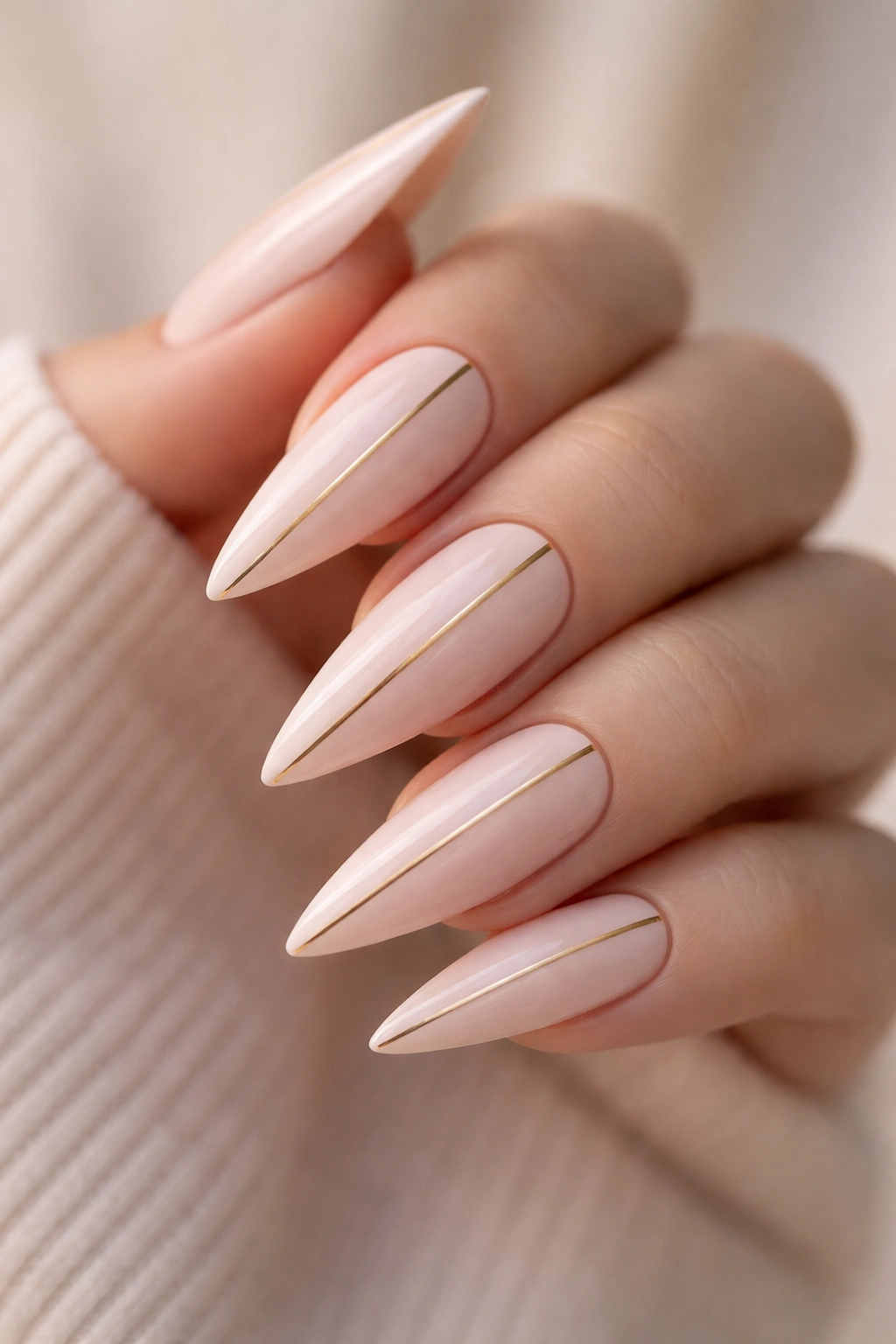 Close-up of pastel blush stiletto nails with thin gold striping