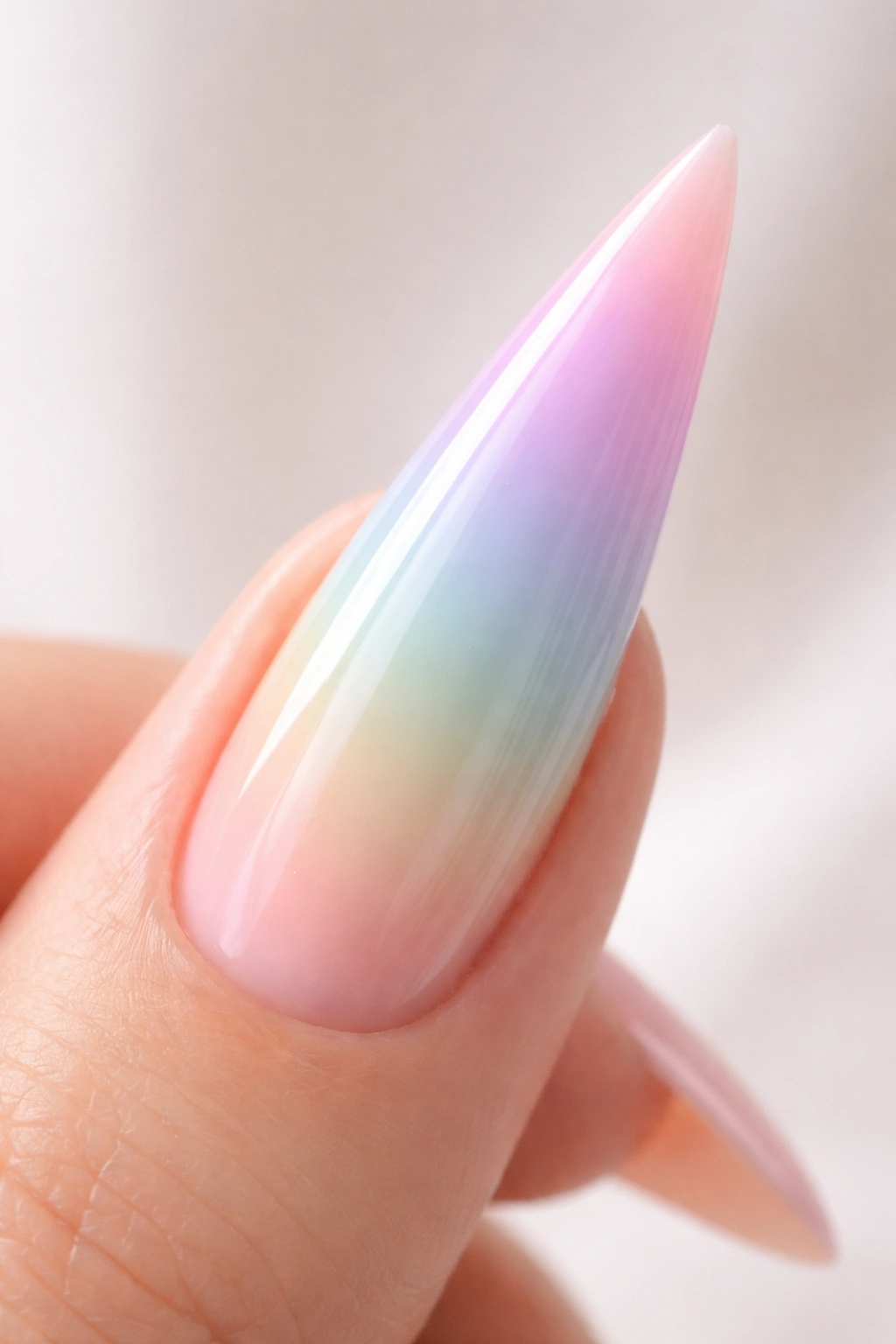 Close-up of a stiletto nail with a soft pastel ombré rainbow gradient on a neutral background