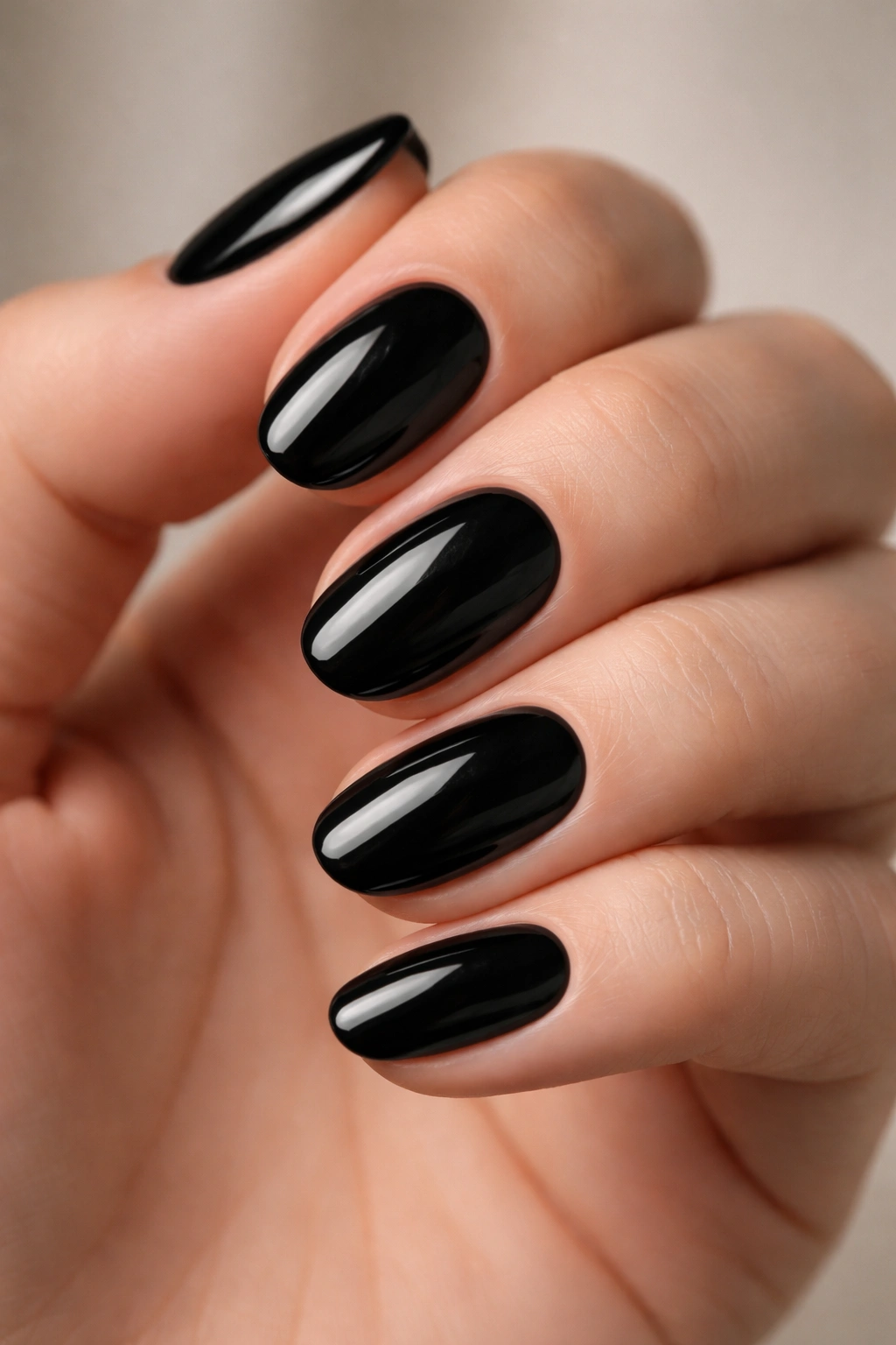 Close-up of short oval nails painted glossy patent black with a smooth surface